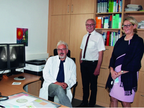 Landrat Dr. Reinhard Kubat und Geschäftsführerin Margarete Janson (beide stehend) ließen sich von Dr. Volker Aßmann die  Diagnostik einer Mammografie-Aufnahme erklären. Alle drei sind vollständig geimpft und haben für die Aufnahme die Masken abgenommen